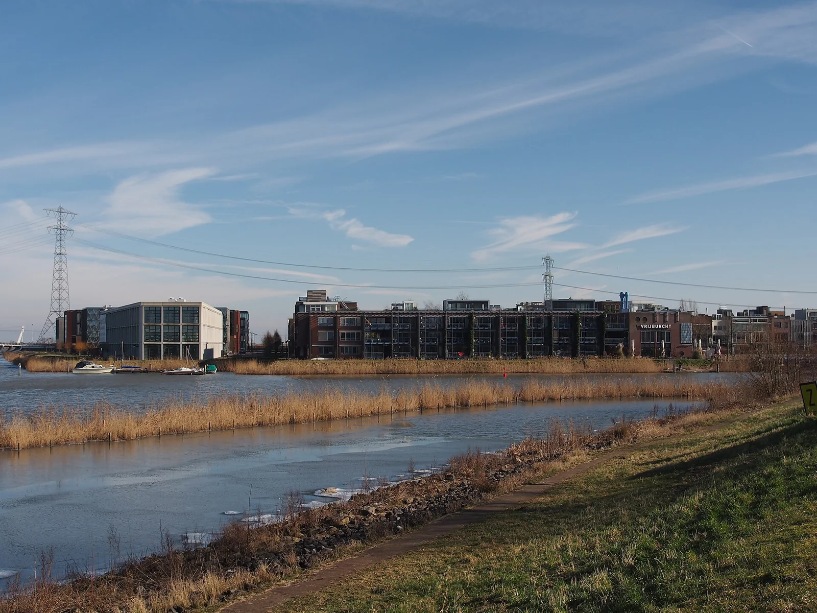 Appartementencomplex met balkons en begroeide gevels aan een rietoever met aanlegsteiger